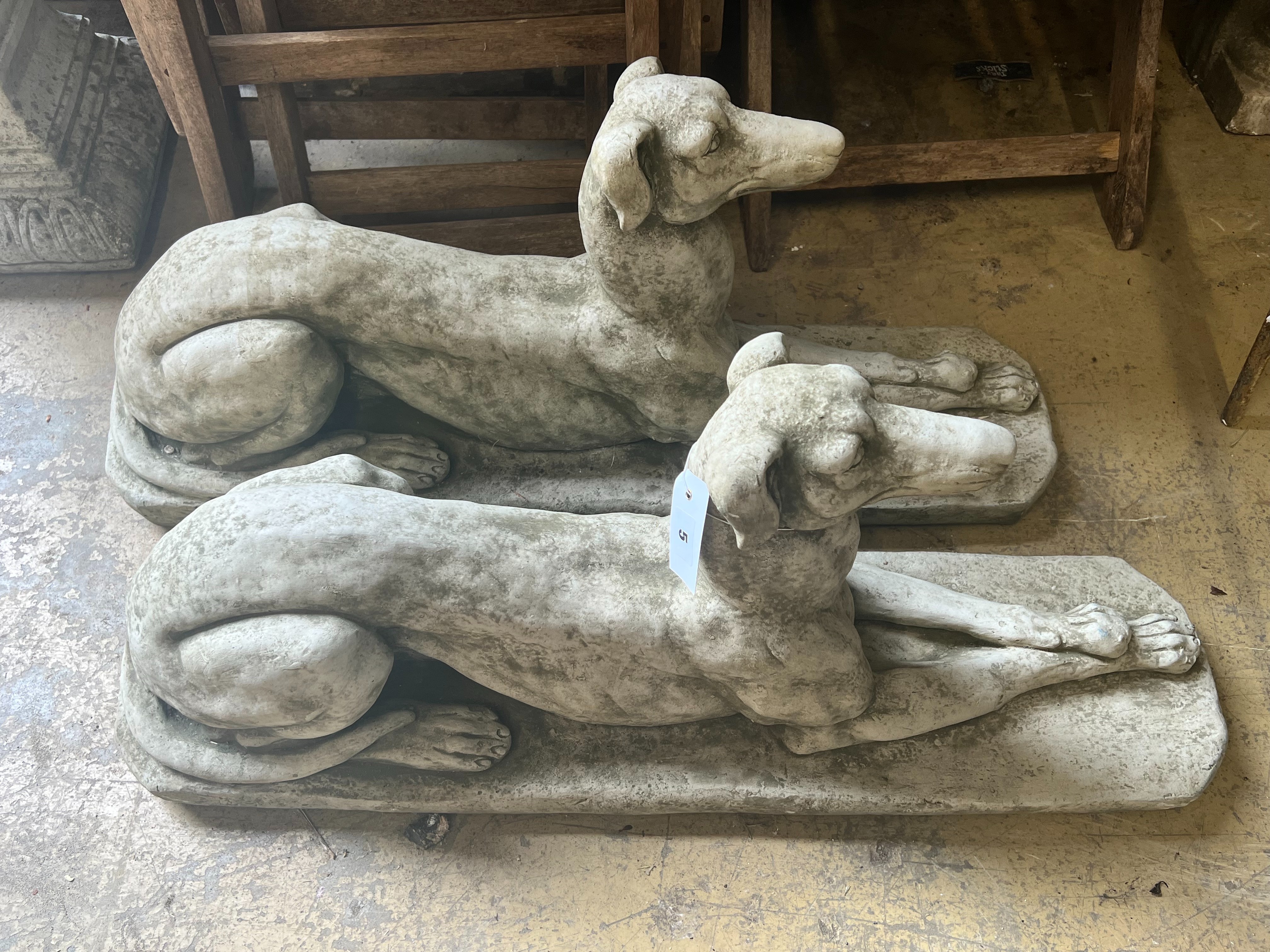 A pair of reconstituted stone recumbent greyhound ornaments, length 82cm